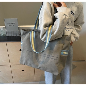 Detail of grey canvas tote bag with vibrant blue and yellow contrast strap and quote