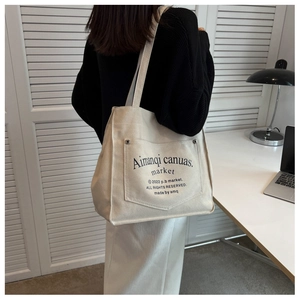Detail of off-white canvas tote bag featuring an outer pocket with black text branding