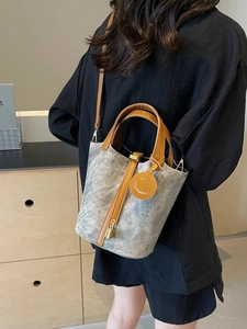Gray canvas bucket bag with brown leather handles and a yellow smiley charm