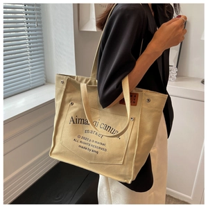 Detail of large canvas tote bag with side metal rivet and brown leather logo patch