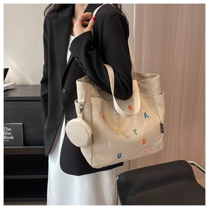 Close-up of beige canvas tote with colorful letter embroidery and round coin purse charm