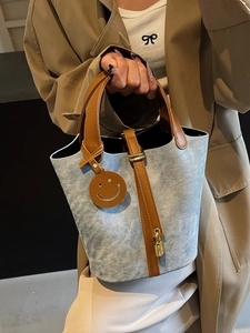 Casual blue denim bucket bag with brown leather handles and a smile charm pendant