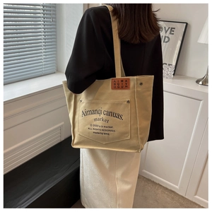 Detail of khaki canvas tote bag with front pocket, metal rivets and vintage lettering print