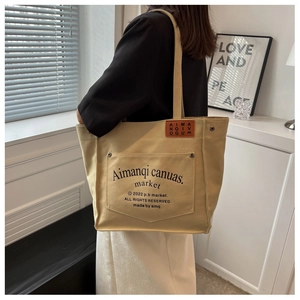 Close-up of beige canvas tote bag detail with metal rivets and envelope outer pocket