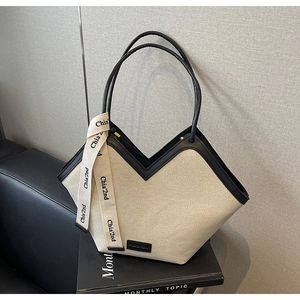Détail du grand sac cabas en toile crème avec coupe en V et brides en cuir noir contrastées