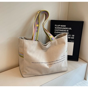 Close-up of beige canvas tote bag with colorful striped straps and minimalist text