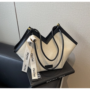 Détail du sac cabas en tissu crème avec ouverture en V, poignées noires et ruban chic