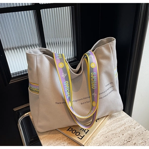 Detail of canvas tote bag with colorful woven handles and minimalist printed text