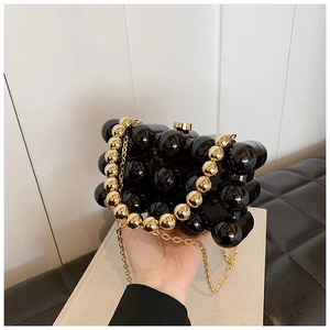 Detail of a black geometric acrylic clutch bag with decorative gold beaded top handle