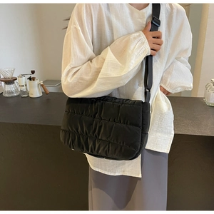 Détail d'un sac bandoulière matelassé noir avec sangle réglable sur un mannequin en blanc