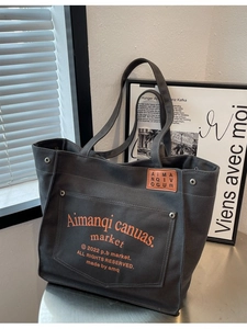 Dark grey canvas tote bag with orange letter print and leather detail on a metal table
