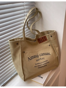 Large khaki canvas tote bag with letter print and leather detail on a sunlit windowsill