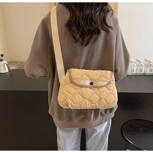 Close-up of beige quilted crossbody bag with soft curved stitching and black button detail