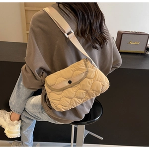 Detail view of cream quilted crossbody bag with wide adjustable strap worn by model