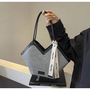 Détail du sac cabas en denim bleu avec anses en cuir noir et ruban de marque