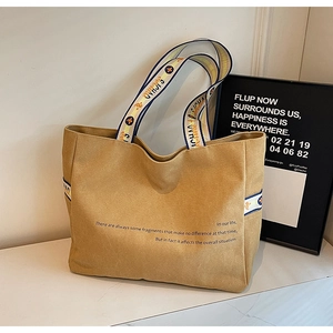 Detail of khaki canvas tote with jacquard strap and letter print on white surface