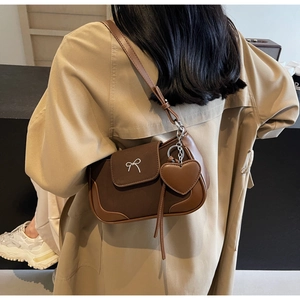 Dettaglio borsa a spalla vintage marrone con fiocco d'argento e ciondolo a cuore su modella