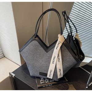 Détail du sac cabas en denim gris avec bords en cuir, ruban décoratif et étiquette mode