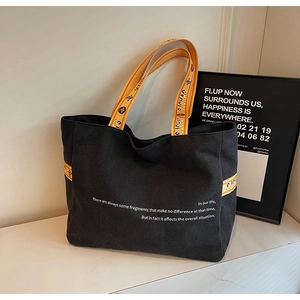 Detailed view of black canvas tote bag with vibrant orange decorative webbing straps