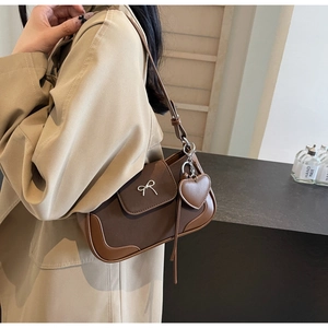 Dettaglio fibbia a fiocco argento e ciondolo a cuore su borsa a tracolla vintage marrone