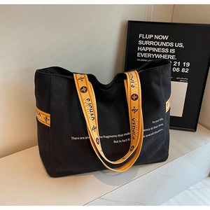 Detail of high-capacity black canvas tote bag with yellow jacquard branded shoulder strap