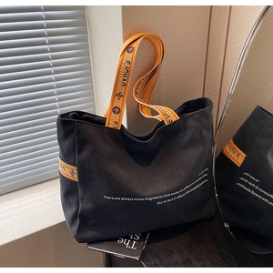 Detail of black canvas tote bag with orange floral jacquard strap and minimalist text