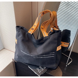 Detail of black canvas tote bag with orange handles and stylish typography design