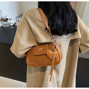 Dettaglio di una borsa a spalla marrone in pelle con fibbia a fiocco e ciondolo cuore