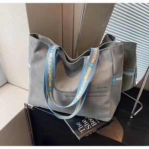 Macro detail of grey canvas tote bag featuring printed slogans and colorful webbed handles