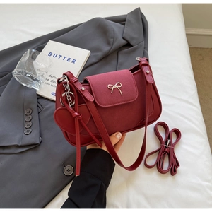 Dettaglio borsa a sella bordeaux con fibbia dorata e ciondolo a cuore su blazer