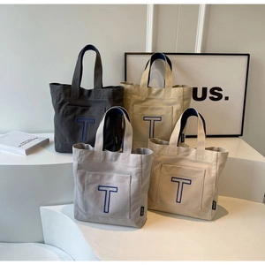 Detail shot of four canvas tote bags in neutral colors with blue T embroidery on a display