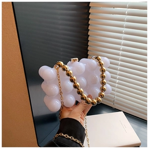 Dettaglio della pochette in acrilico bianco con manico di perle dorate e catena