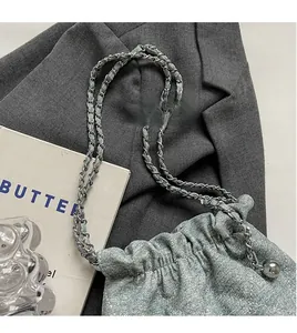 Detail of light blue denim bucket bag with silver metal chain strap and drawstring closure