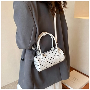 French style white polka dot barrel bag worn crossbody by a model in a grey blazer