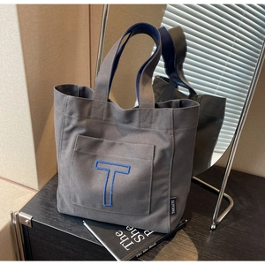 Detail of grey canvas tote bag featuring blue embroidered T and brand woven label