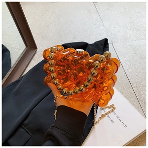 Dettaglio borsa da sera in acrilico arancione con onde, perle dorate e catenella