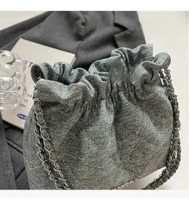 Detail of blue denim bucket bag with quilted patterns and silver chain strap on grey fabric