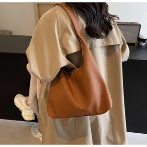 Detailed close-up of a caramel brown lychee leather tote bag worn with a beige trench coat