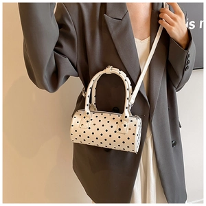 Close-up of a white cylindrical Boston bag with black polka dots and dual top handles