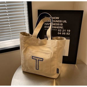 Detail of canvas tote bag featuring blue letter T embroidery and brand label on side