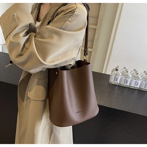Nahaufnahme der braunen Eimer-Tasche aus Litchi-Leder mit Logoprägung und Schultergurt