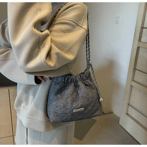 Detail of grey denim bucket bag with quilted stitching and metallic chain strap worn by model