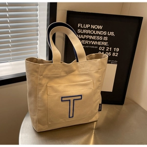 Detail of canvas tote bag showing exterior pocket with blue T embroidery and shoulder straps