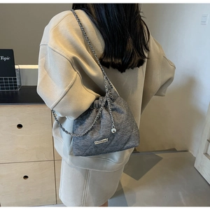 Detailed view of grey quilted tweed bucket bag with silver chain strap on model