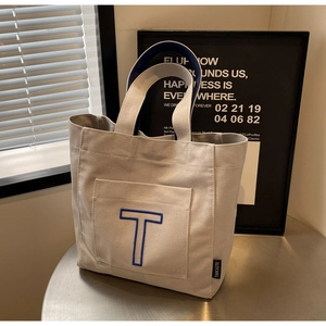 Detail of canvas tote bag featuring large blue embroidered letter T and durable handle