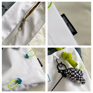 Detailed view of white tote bag with smooth metal zipper, neon green rope and charm