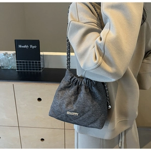 Detail of grey quilted denim bucket bag featuring chain strap and drawstring closure