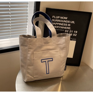 Detail of grey canvas tote bag featuring blue letter T patch and contrast handles