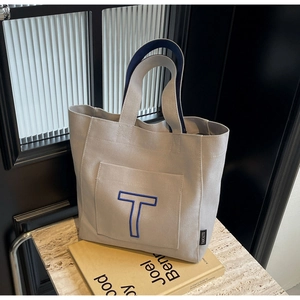 Close-up of canvas tote bag showing embroidered blue letter T and durable handle details