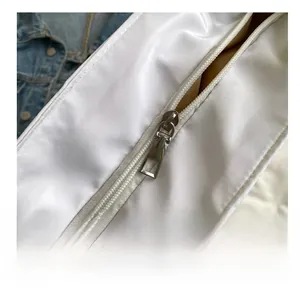 Macro shot of smooth metal zipper detail on white nylon tote bag with denim background